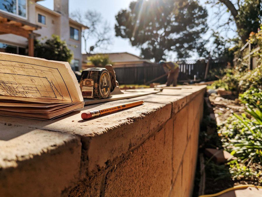 A site plan, a tape measure and a pencil on the cap of a block wall