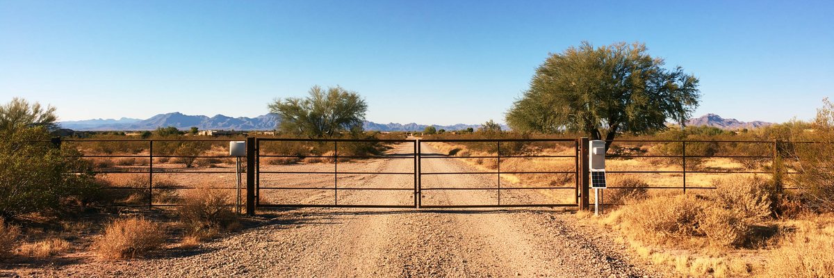 A steel driveway gate with a solar panel and control box at a rural drive, Queen Creek, AZ.