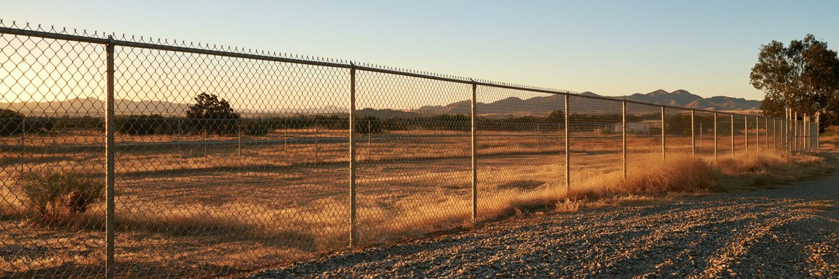 A chain link fence with a barbed wire top running along open ground, Queen Creek, AZ.
