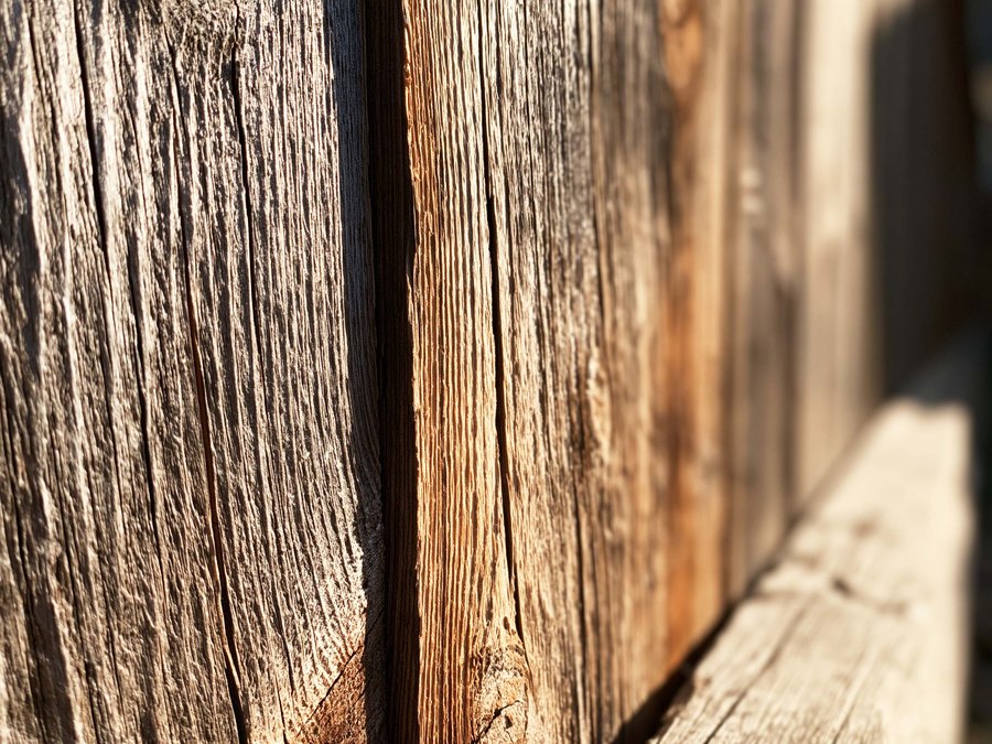 Weathered cedar boards where the sun has opened splits along the grain