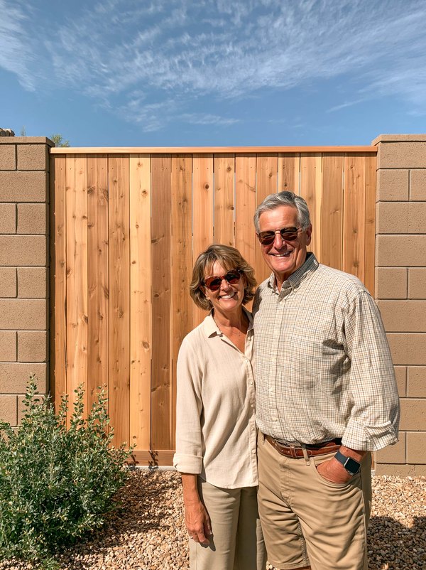Two homeowners in front of a new cedar fence built in between two block walls